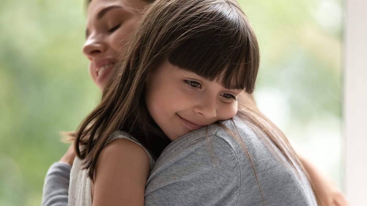 Adopted girl on mothers shoulder feeling love and supported.