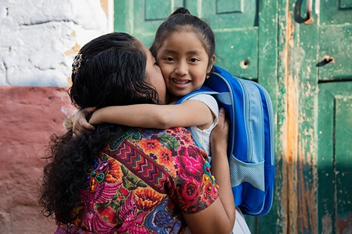 Young girl smiling while hugging a woman outside a building, symbolizing the impact of CityServe’s Compassion Initiatives to support families and build stronger communities.