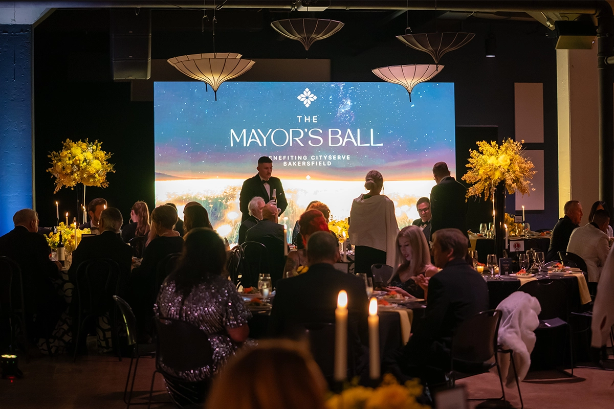Guests seated at tables with The Mayor’s Ball event stage screen in the background.